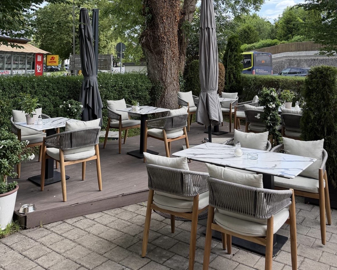 Gemütliche Terrasse mit Marmortischen und Rattanstühlen vor dem Café
